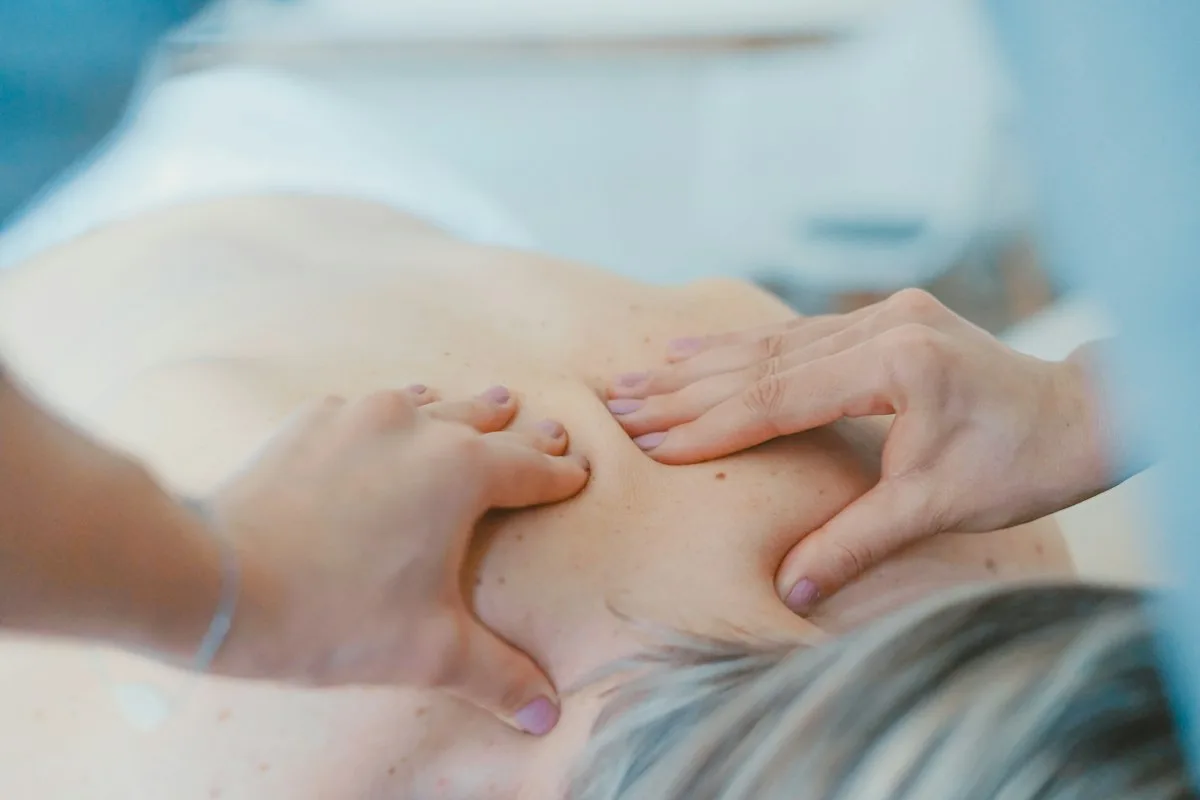 Hände einer Therapeutin arbeiten am Rücken eines liegenden Patienten